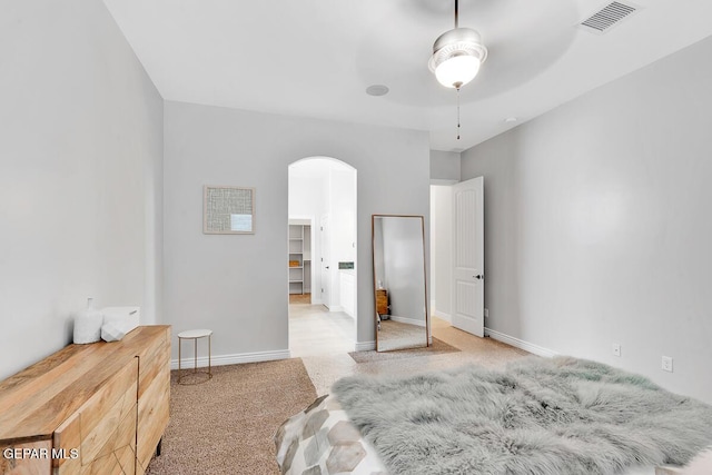 carpeted bedroom featuring a walk in closet and ceiling fan