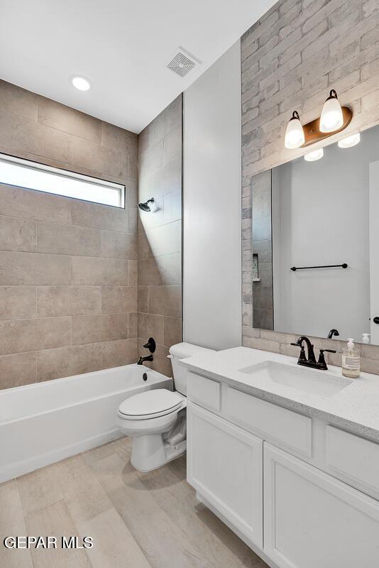 full bathroom featuring vanity, tiled shower / bath combo, and toilet