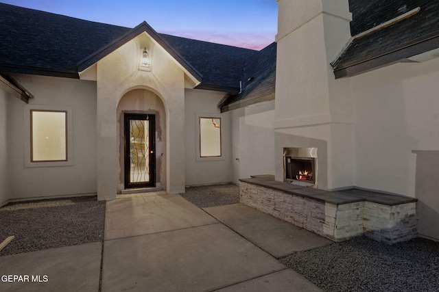 exterior entry at dusk with a patio and an outdoor fireplace