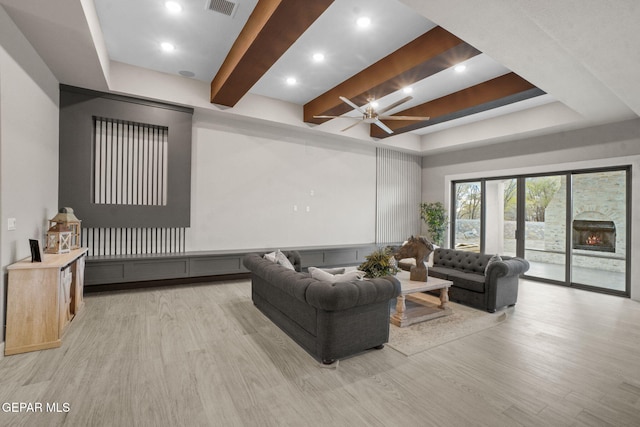 living room with a tray ceiling, ceiling fan, a fireplace, and light wood-type flooring