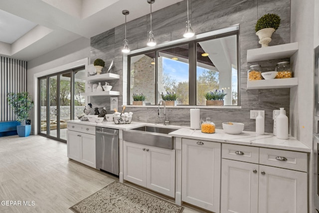 kitchen featuring light stone countertops, white cabinetry, sink, stainless steel dishwasher, and pendant lighting