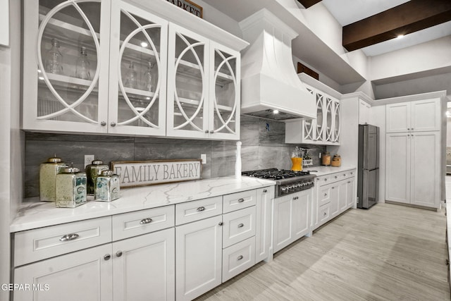 kitchen with backsplash, premium range hood, white cabinetry, and stainless steel appliances