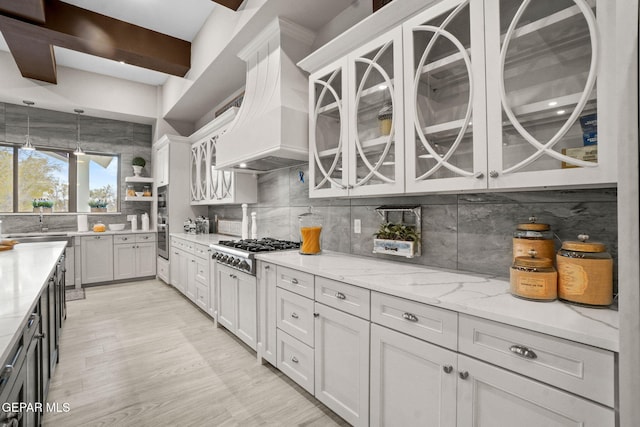 kitchen with light stone countertops, backsplash, custom exhaust hood, stainless steel gas cooktop, and white cabinets