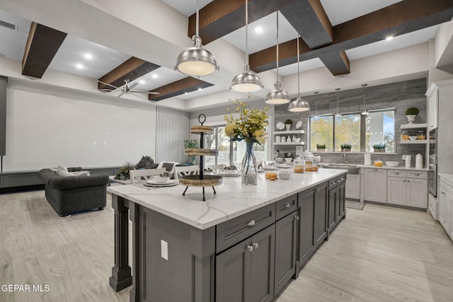 kitchen with light stone counters, stainless steel oven, ceiling fan, a spacious island, and decorative light fixtures