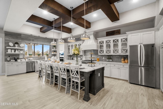 kitchen featuring white cabinets, stainless steel appliances, premium range hood, and a kitchen island with sink