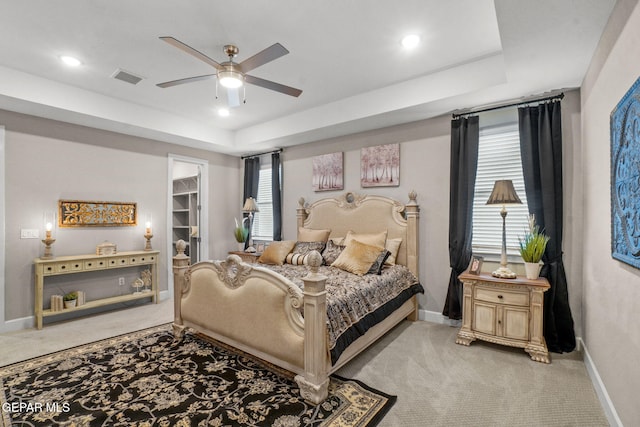 carpeted bedroom featuring a raised ceiling, a walk in closet, ceiling fan, and a closet