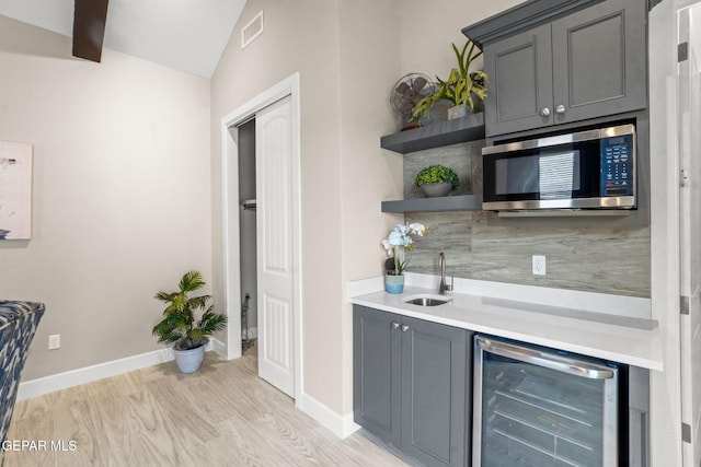 bar with sink, beverage cooler, light hardwood / wood-style floors, gray cabinets, and decorative backsplash