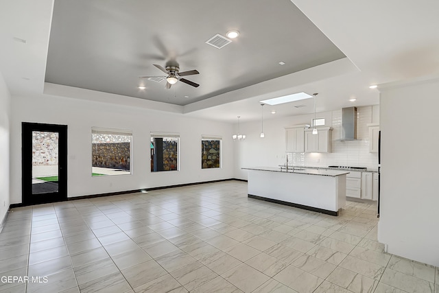 kitchen featuring a tray ceiling, white cabinetry, hanging light fixtures, and wall chimney range hood