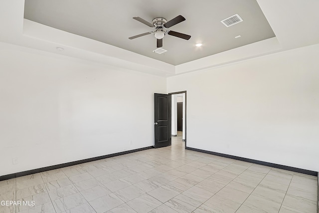 tiled empty room featuring a raised ceiling and ceiling fan