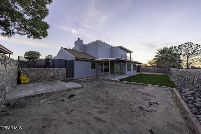 back house at dusk with a patio and a lawn