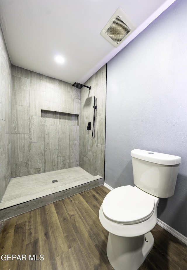 bathroom featuring a tile shower, hardwood / wood-style floors, and toilet