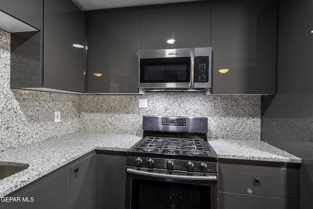 kitchen featuring gray cabinetry, decorative backsplash, light stone counters, and stainless steel appliances