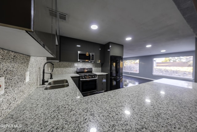 kitchen featuring light stone countertops, sink, kitchen peninsula, decorative backsplash, and appliances with stainless steel finishes