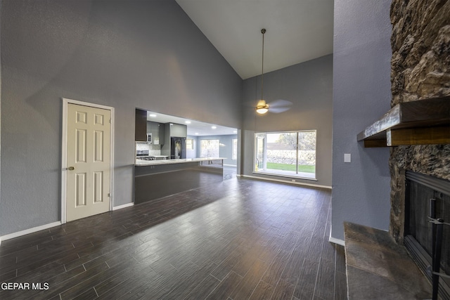 unfurnished living room with dark hardwood / wood-style flooring, high vaulted ceiling, ceiling fan, and a stone fireplace