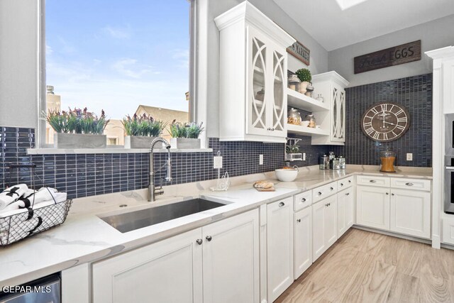 kitchen featuring light stone countertops, white cabinetry, plenty of natural light, and sink