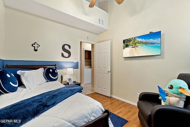 bedroom featuring ceiling fan, a high ceiling, washer / clothes dryer, and light hardwood / wood-style flooring