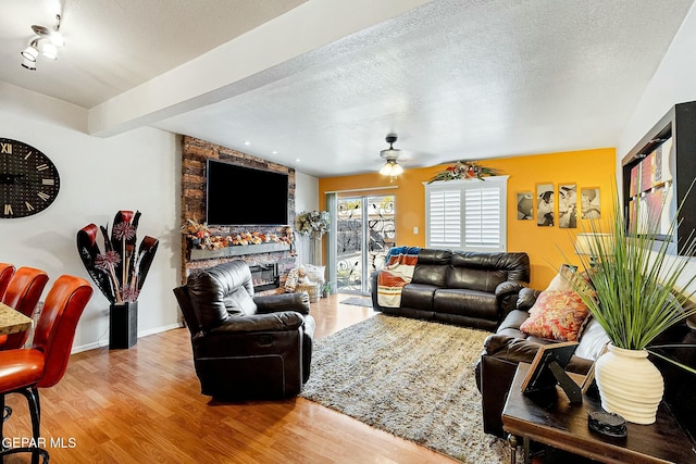 living room with hardwood / wood-style floors, a textured ceiling, a stone fireplace, and ceiling fan