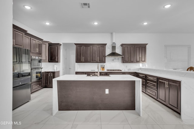 kitchen featuring wall chimney exhaust hood, sink, tasteful backsplash, dark brown cabinets, and appliances with stainless steel finishes