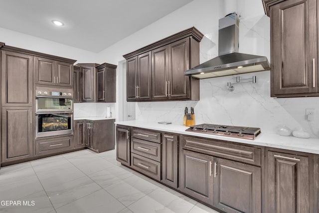 kitchen featuring appliances with stainless steel finishes, dark brown cabinets, wall chimney range hood, and decorative backsplash