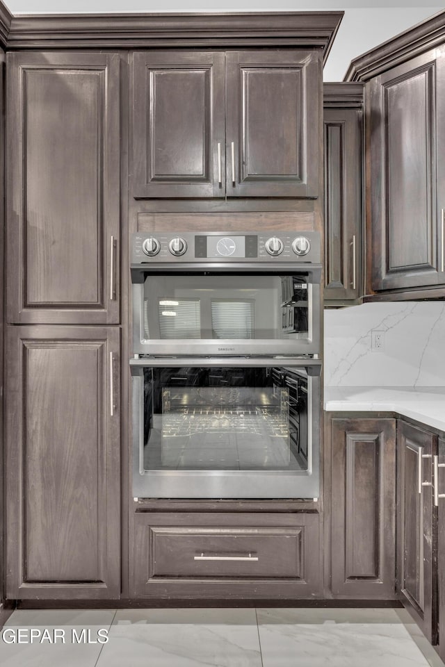 kitchen with dark brown cabinets, light stone counters, backsplash, and double oven