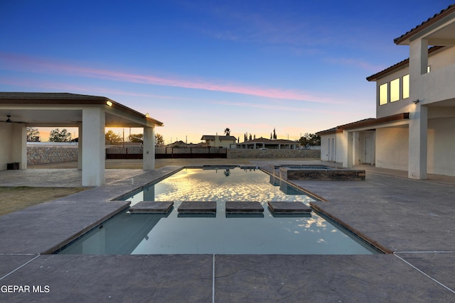 pool at dusk with an in ground hot tub and a patio area