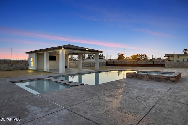 pool at dusk with a patio and an in ground hot tub