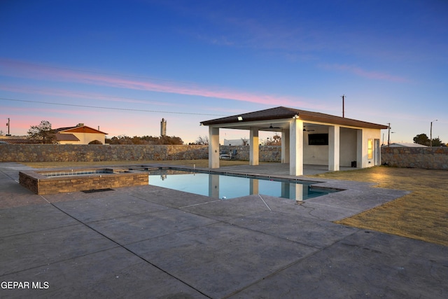 pool at dusk featuring a patio area, ceiling fan, and an in ground hot tub