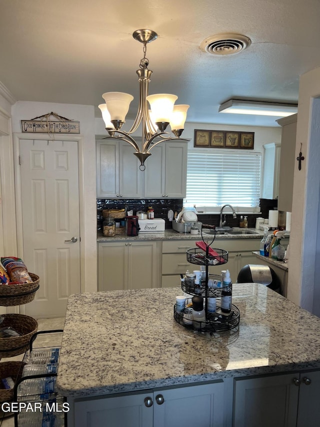 kitchen featuring light stone countertops, sink, pendant lighting, an inviting chandelier, and a kitchen island