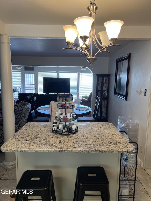 kitchen with a kitchen bar, ornate columns, a notable chandelier, hanging light fixtures, and light tile patterned flooring