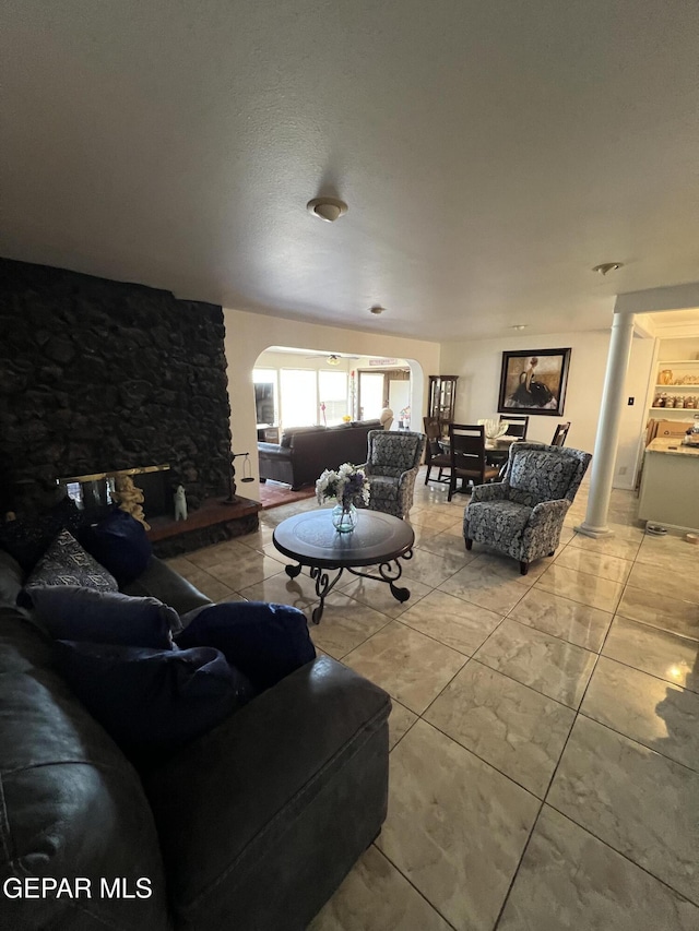 living room featuring decorative columns and a stone fireplace