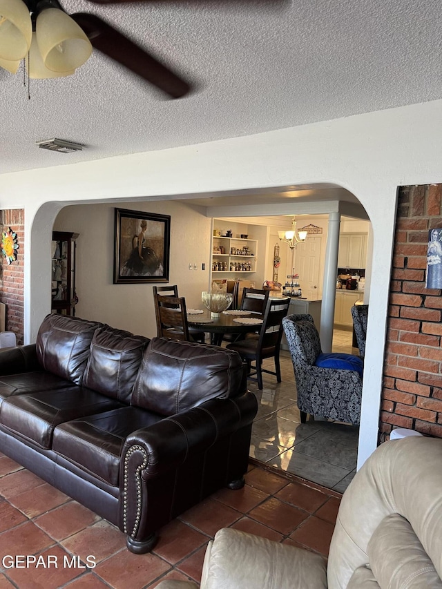 tiled living room featuring ceiling fan with notable chandelier and a textured ceiling