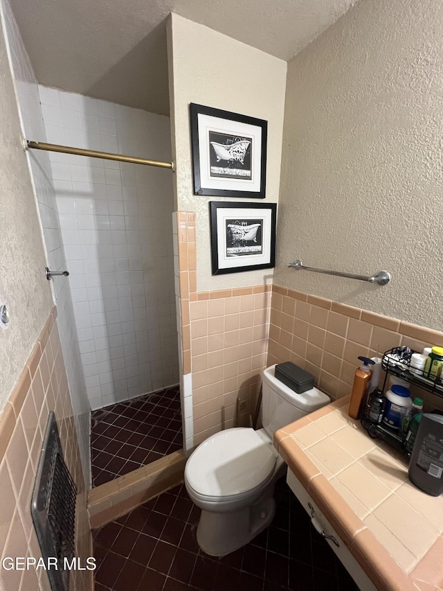 bathroom featuring tile patterned floors, a textured ceiling, tiled shower, tile walls, and toilet