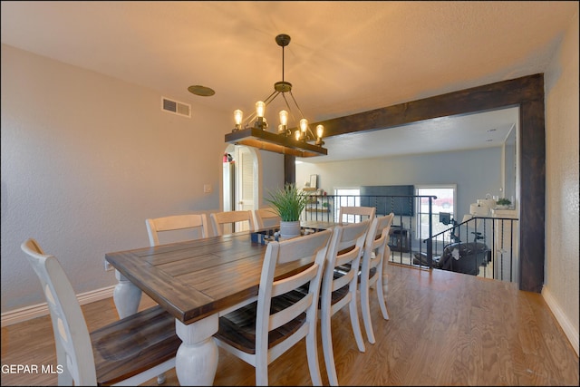 dining area featuring hardwood / wood-style flooring, a notable chandelier, and beamed ceiling