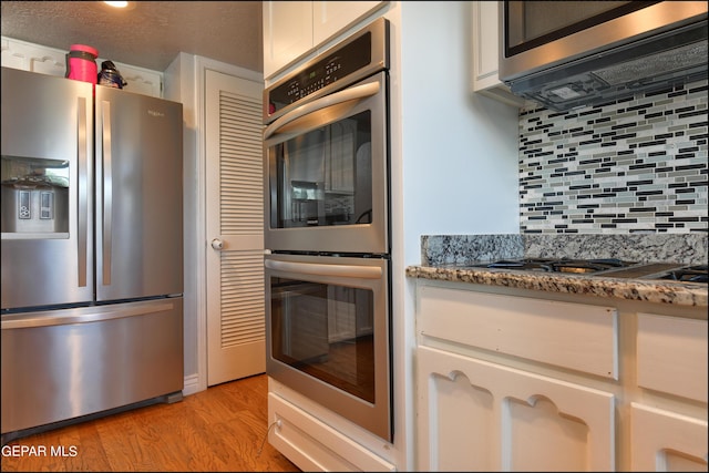 kitchen with dark stone countertops, light wood-type flooring, appliances with stainless steel finishes, tasteful backsplash, and white cabinetry