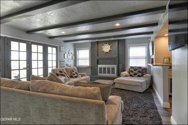 living room featuring a healthy amount of sunlight, wood-type flooring, a textured ceiling, and a brick fireplace