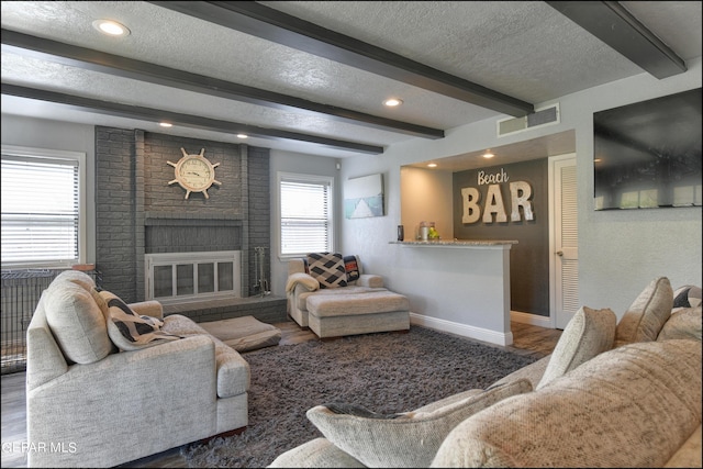 living room featuring beamed ceiling, dark wood-type flooring, a textured ceiling, and a brick fireplace