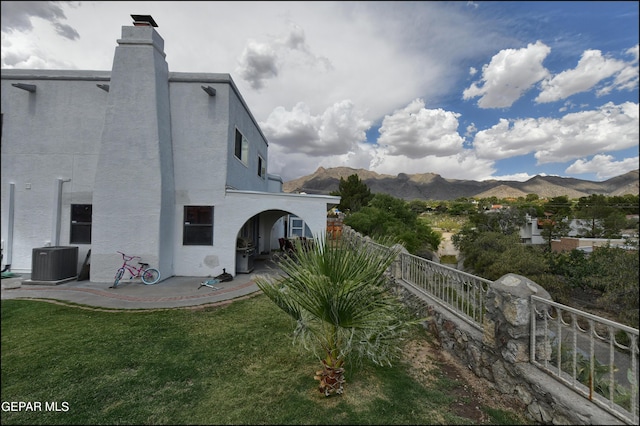 view of property exterior with a mountain view, cooling unit, a patio area, and a yard