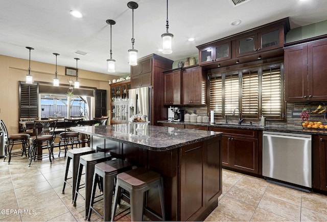 kitchen with dark stone counters, sink, hanging light fixtures, a kitchen island, and stainless steel appliances