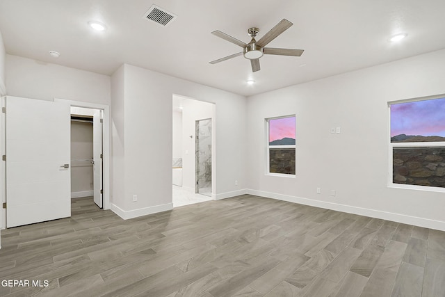 unfurnished bedroom with a spacious closet, light hardwood / wood-style flooring, ensuite bath, and ceiling fan