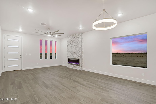 unfurnished living room featuring wood-type flooring, heating unit, ceiling fan, and a high end fireplace