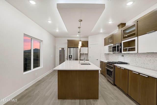 kitchen featuring light wood-type flooring, stainless steel appliances, sink, a center island with sink, and hanging light fixtures