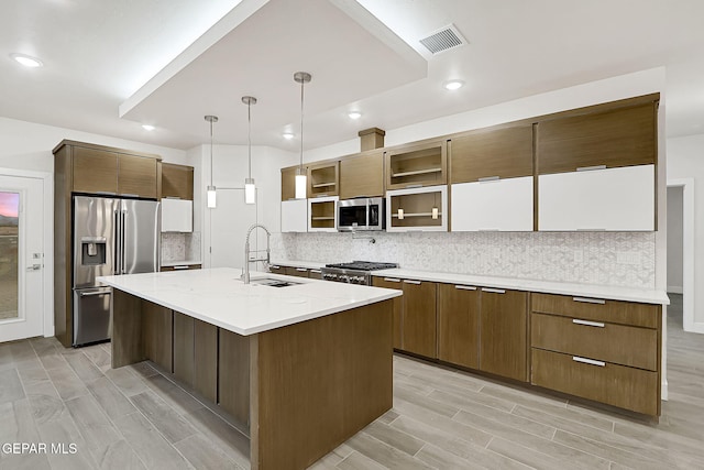 kitchen with a kitchen island with sink, sink, hanging light fixtures, tasteful backsplash, and stainless steel appliances