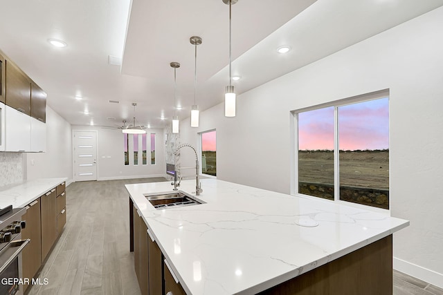 kitchen with light wood-type flooring, ceiling fan, sink, hanging light fixtures, and a large island