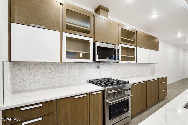 kitchen featuring stainless steel appliances, white cabinetry, backsplash, and light stone counters