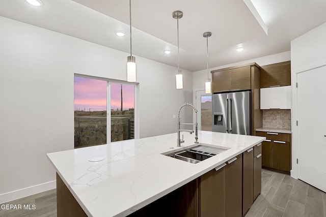 kitchen with a center island with sink, decorative light fixtures, high end fridge, and sink