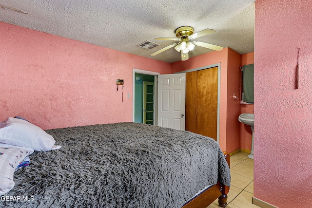 bedroom featuring ceiling fan, light tile patterned floors, a textured ceiling, connected bathroom, and a closet