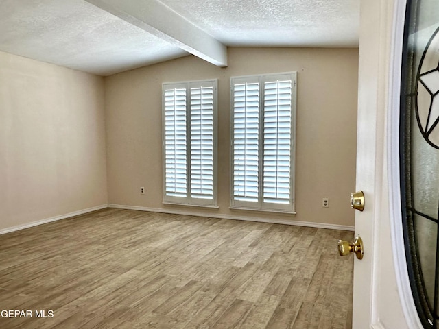 empty room featuring a textured ceiling, lofted ceiling with beams, and light hardwood / wood-style flooring