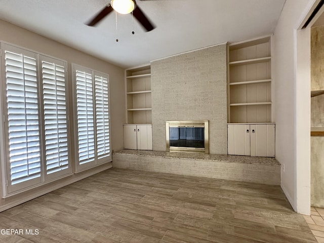 unfurnished living room featuring built in features, light hardwood / wood-style floors, a brick fireplace, and ceiling fan