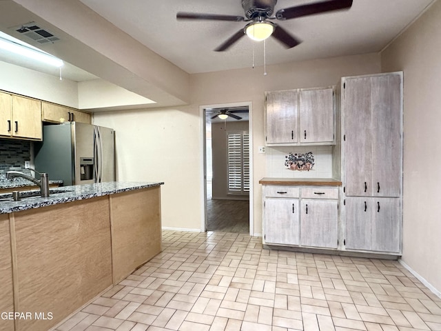 kitchen with decorative backsplash, stainless steel fridge, sink, and light stone countertops