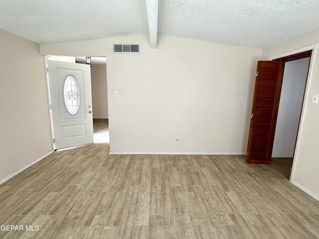 entryway with lofted ceiling with beams, light hardwood / wood-style floors, and a textured ceiling